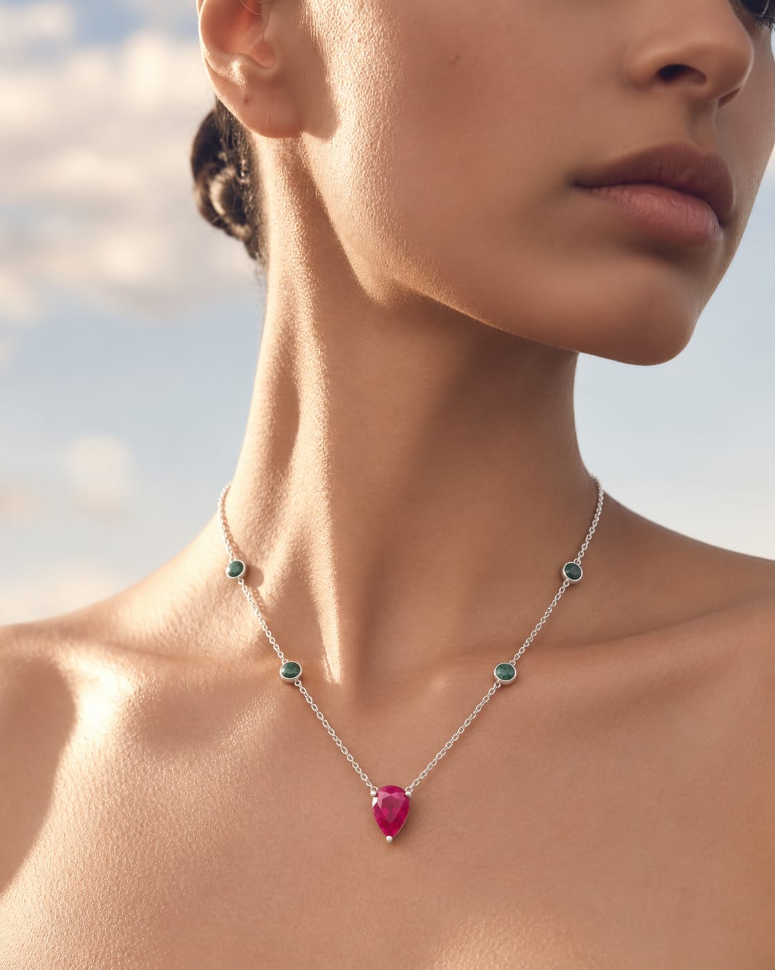 Silver-coloured necklace with round green accents and a pink pear-shaped pendant, worn at the neckline in sunlight.