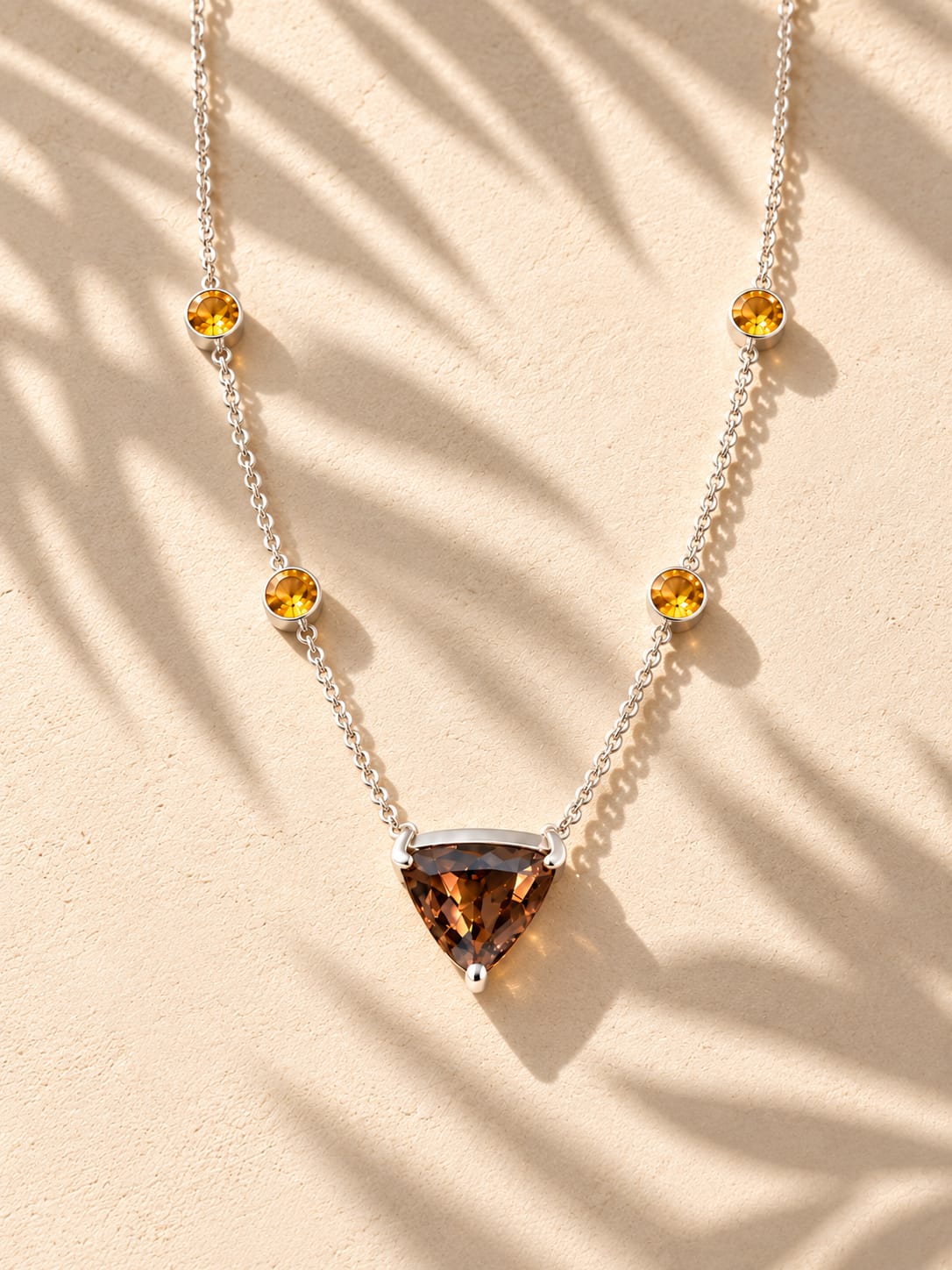 Brown triangular pendant and golden-coloured round accents on a silver-coloured chain, photographed in warm sunlight.
